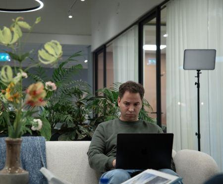 Een collega werkt op zijn laptop op een bank in een loungeruimte